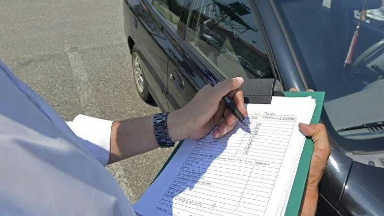 Photograph of a driving test examiner stood next to a car with a marksheet