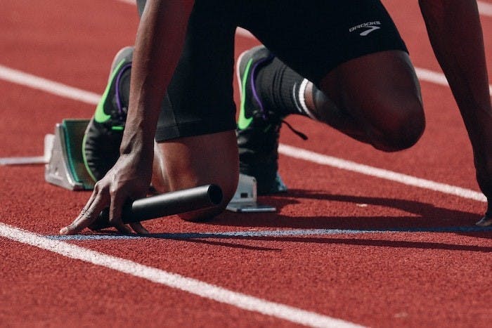 Photograph of a relay racer crouched down on a track and ready to start the race.