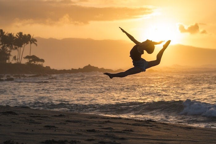 Photograph of a woman performing acrobatics on a beach during sunset