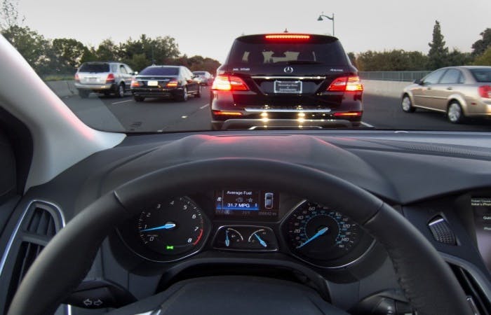 Photograph taken from the driver's perspective of a car performing an emergency stop. The car in front's brake lights are illuminated.