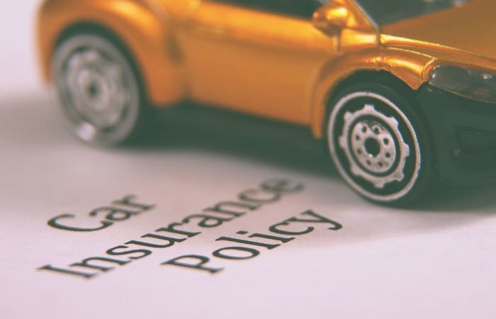 Close up of a toy car on top of a piece of paper with text that reads "car insurance policy"