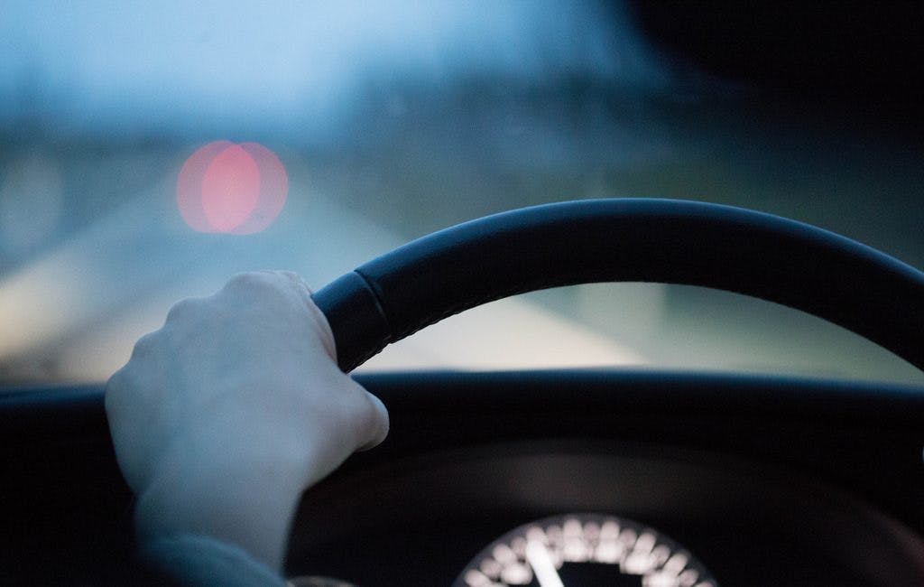 An image of a persons hand on a steering wheel while driving a car 