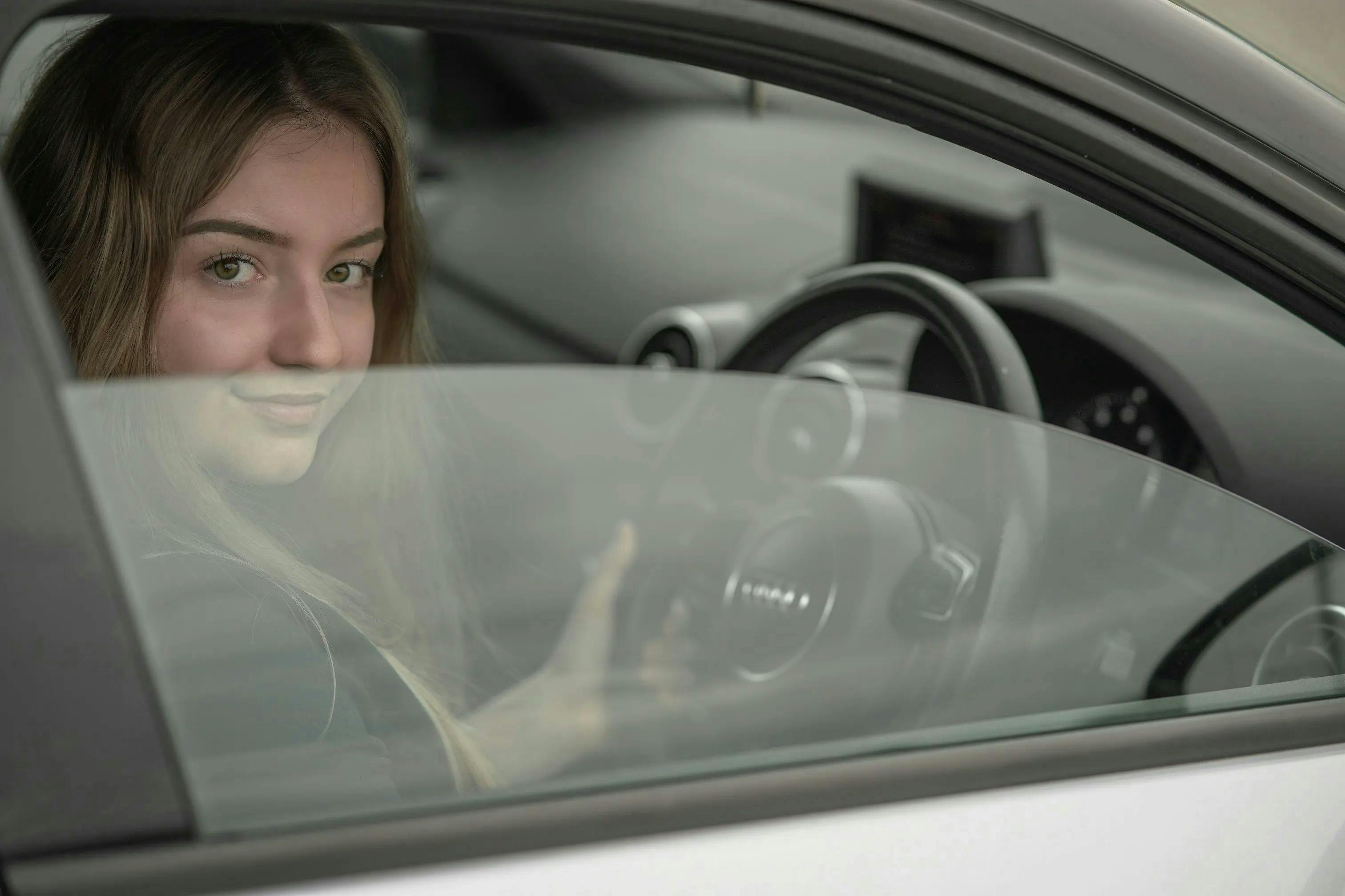A young woman glancing out of the window of a car as she sits in the driver's seat