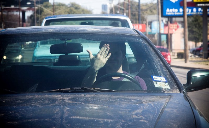 Man sat in dirty car waving hand in annoyed manner