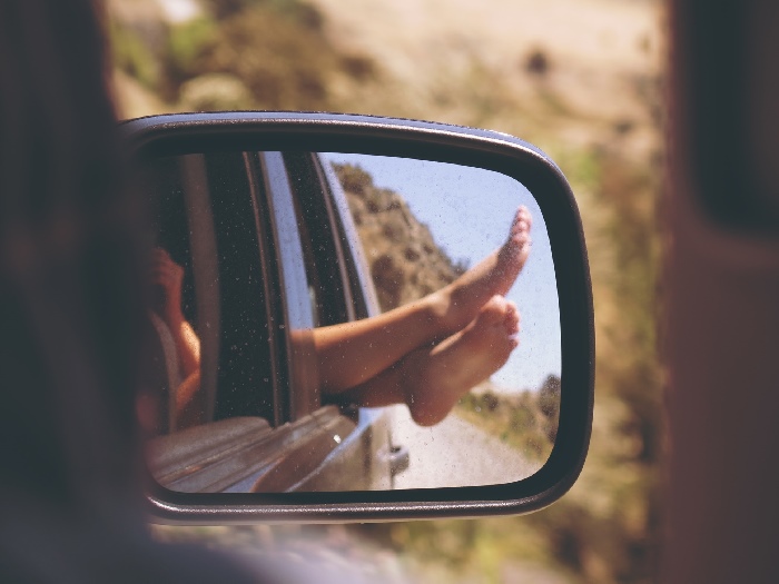 Bare feet poking out of car window seen through wing mirror