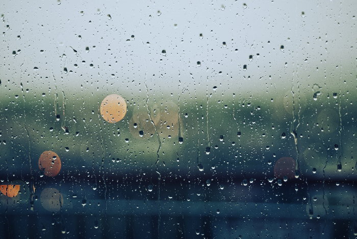 Close up of window covered in rain drops with blurred background