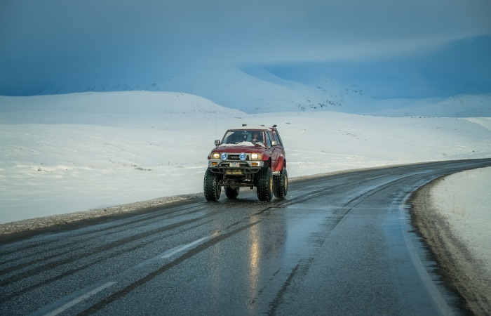 red-suv-on-empty-road-with-snow-in-background