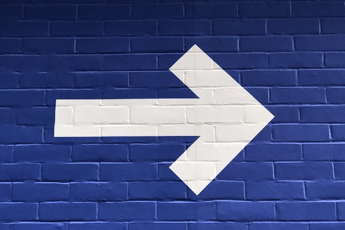 White arrow pointing right painted on blue brick wall